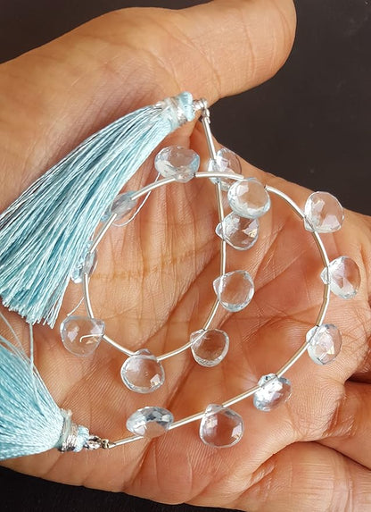 A person holding a strand of sky blue topaz faceted heart beads, showcasing their natural beauty and shine.