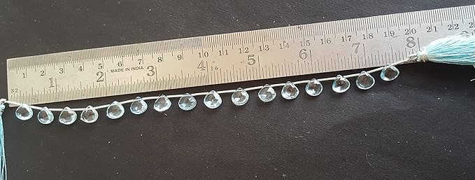  A close-up of a ruler measuring a strand crafted from sky blue topaz faceted heart gemstone beads.