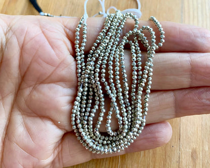 A person holding a strand of sliver pyrite faceted rondelle beads, showcasing their natural beauty and shine.
