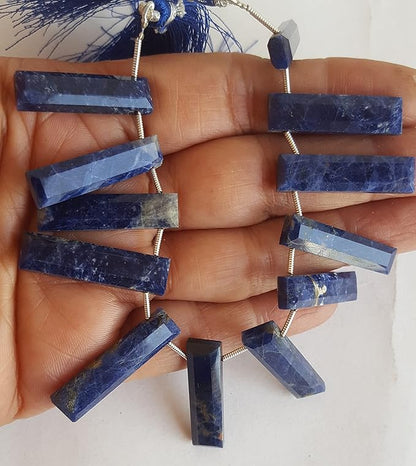 A hand holds a stunning blue strand made of faceted  Sodalite briolette gemstones.