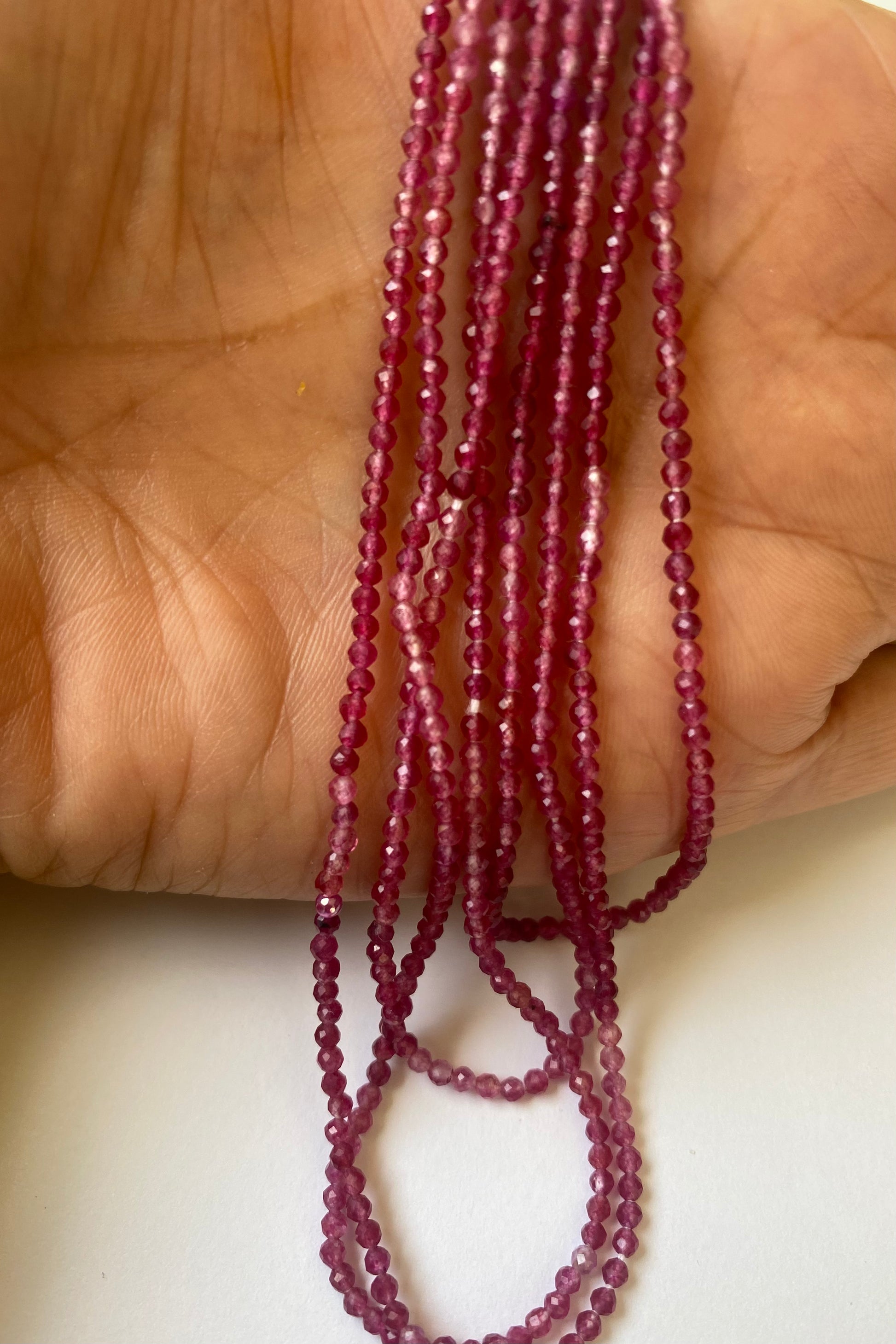A hand displays a strand of 2-2.2mm Strawberry Quartz, emphasising their classic beauty and refined style.