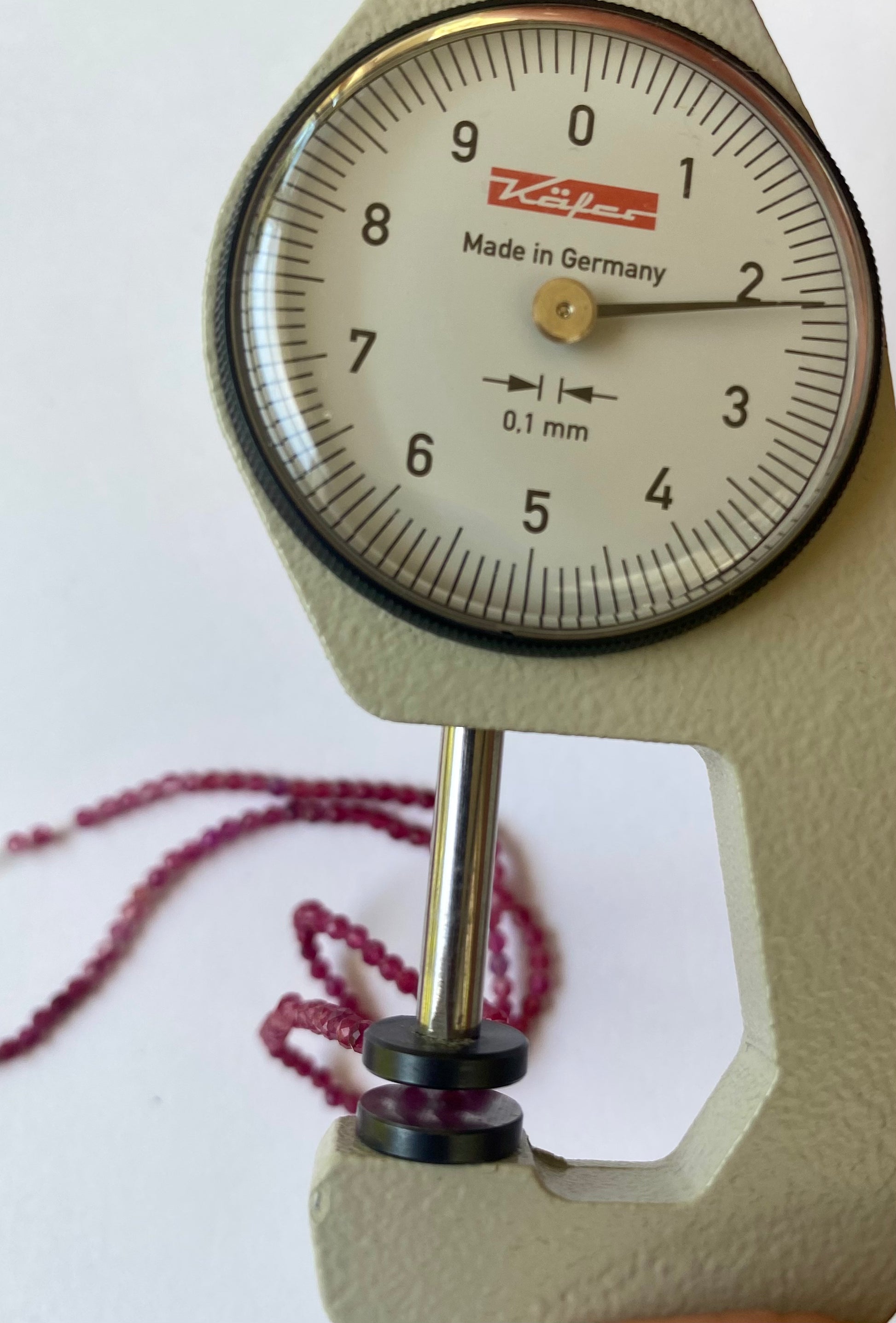 A dial gauge with a 2-2.2mm Strawberry Quartz strand resting on it, emphasising the size and measurement.