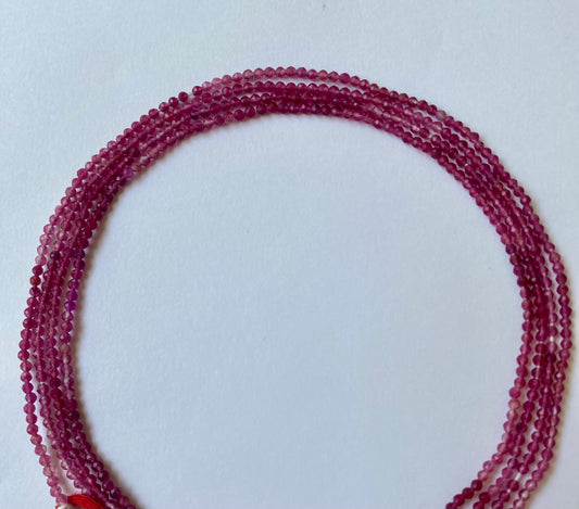 Strands of micro-faceted pink strawberry quartz beads, 2-2.2mm, elegantly displayed on a smooth white surface.