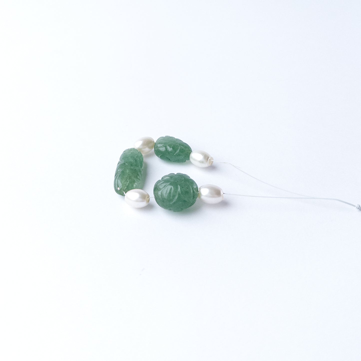 Close‑up of Green Strawberry Quartz and Shell Pearl beads highlighting their carved texture and shape.
