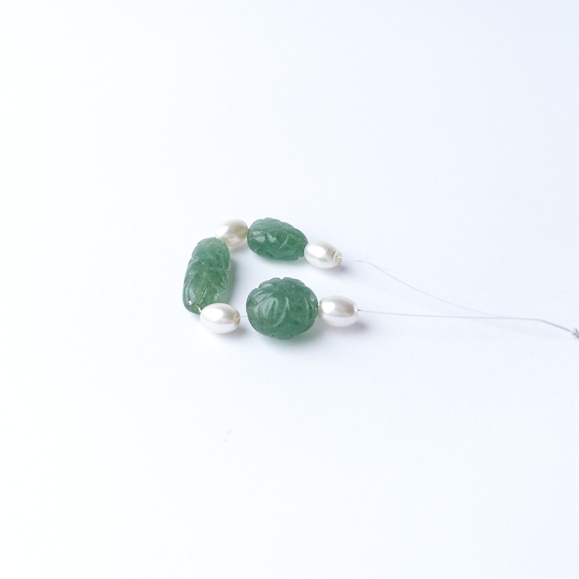Close‑up of Green Strawberry Quartz and Shell Pearl beads highlighting their carved texture and shape.