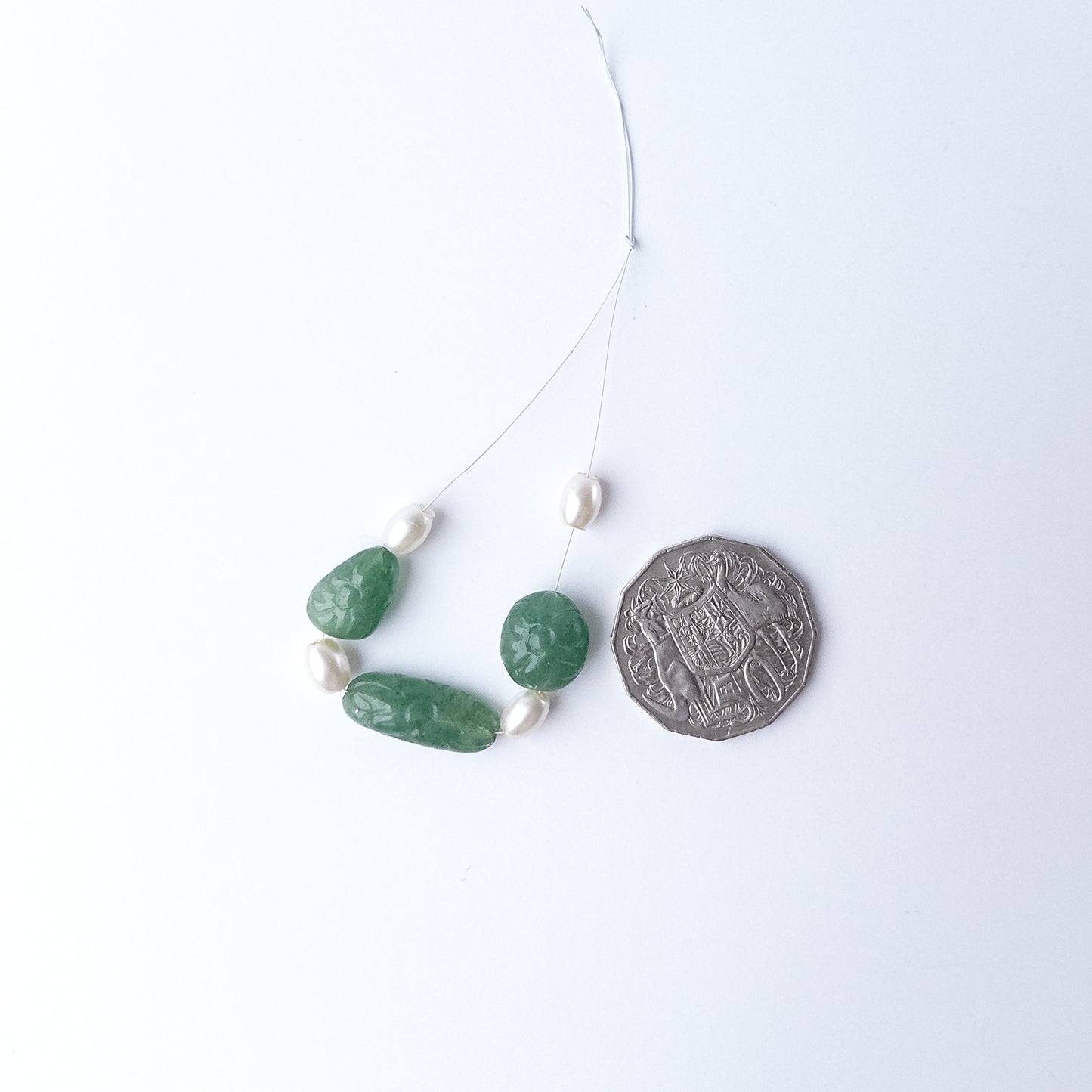 A coin is placed near delicate pieces of Green Strawberry Quartz and Shell Pearl beads for scale.