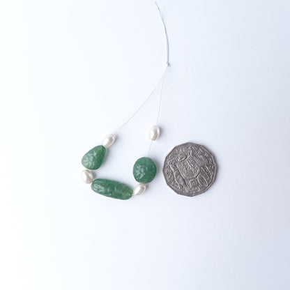 A coin is placed near delicate pieces of Green Strawberry Quartz and Shell Pearl beads for scale.