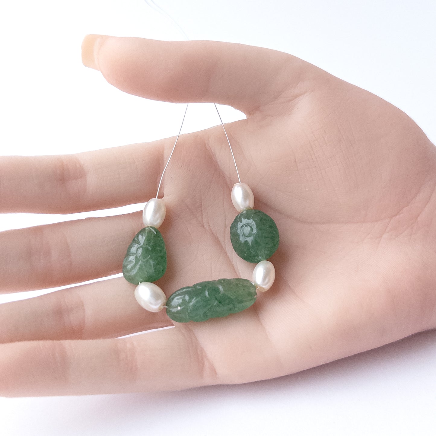 A person holds delicate pieces of Green Strawberry Quartz and Shell Pearl beads, showcasing their carved tumble design.