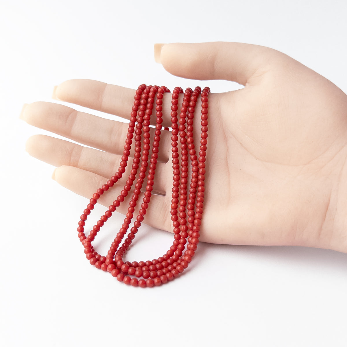 A person holds delicate strands of Taiwan Coral beads, showcasing their smooth round design.