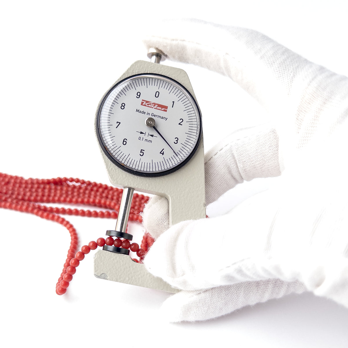 A dial gauge measures the Taiwan Coral Smooth Round 3.5mm gemstone.