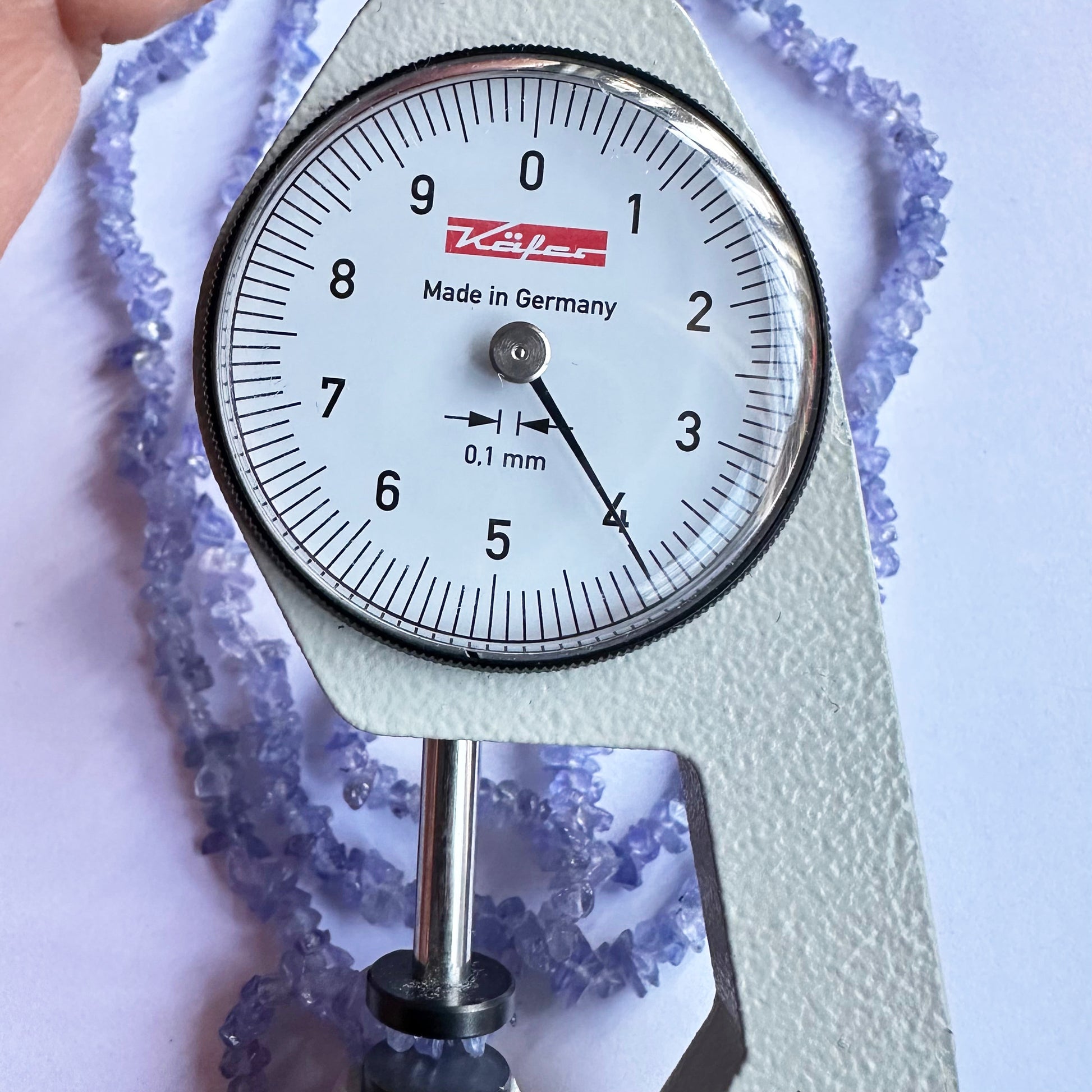 A dial gauge measures the Tanzanite uncut chip beads, verifying their 3.5-5mm size for precision in jewelry-making