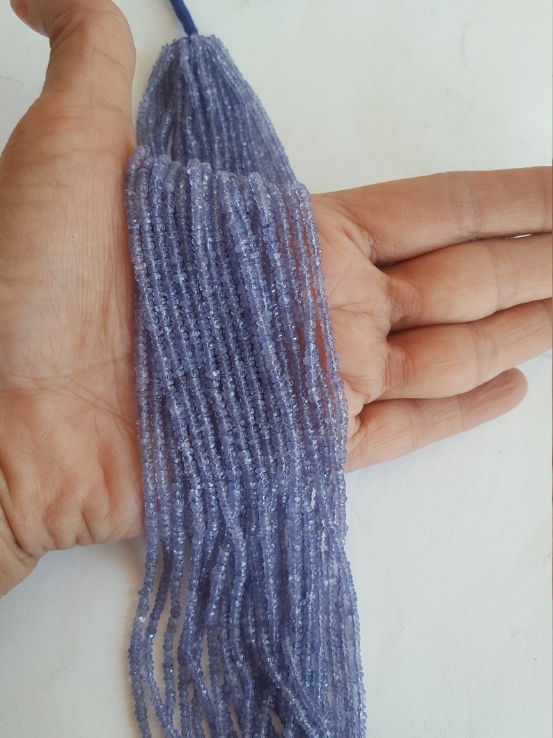 A person holding a strands of faceted tanzanite rondelle precious gemstone beads, showcasing their vibrant colour and shine.