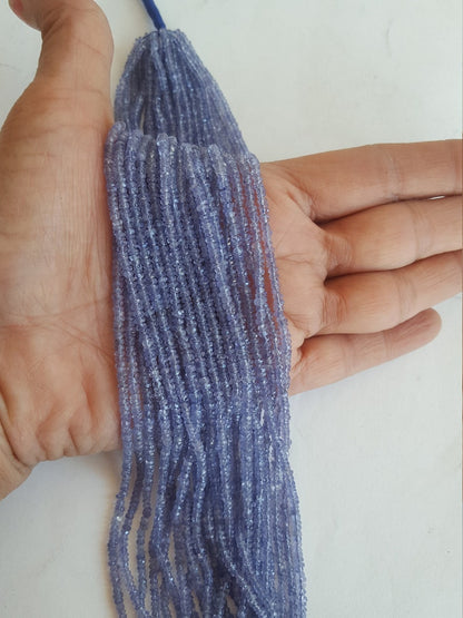 A person holding a strands of faceted tanzanite rondelle precious gemstone beads, showcasing their vibrant colour and shine.