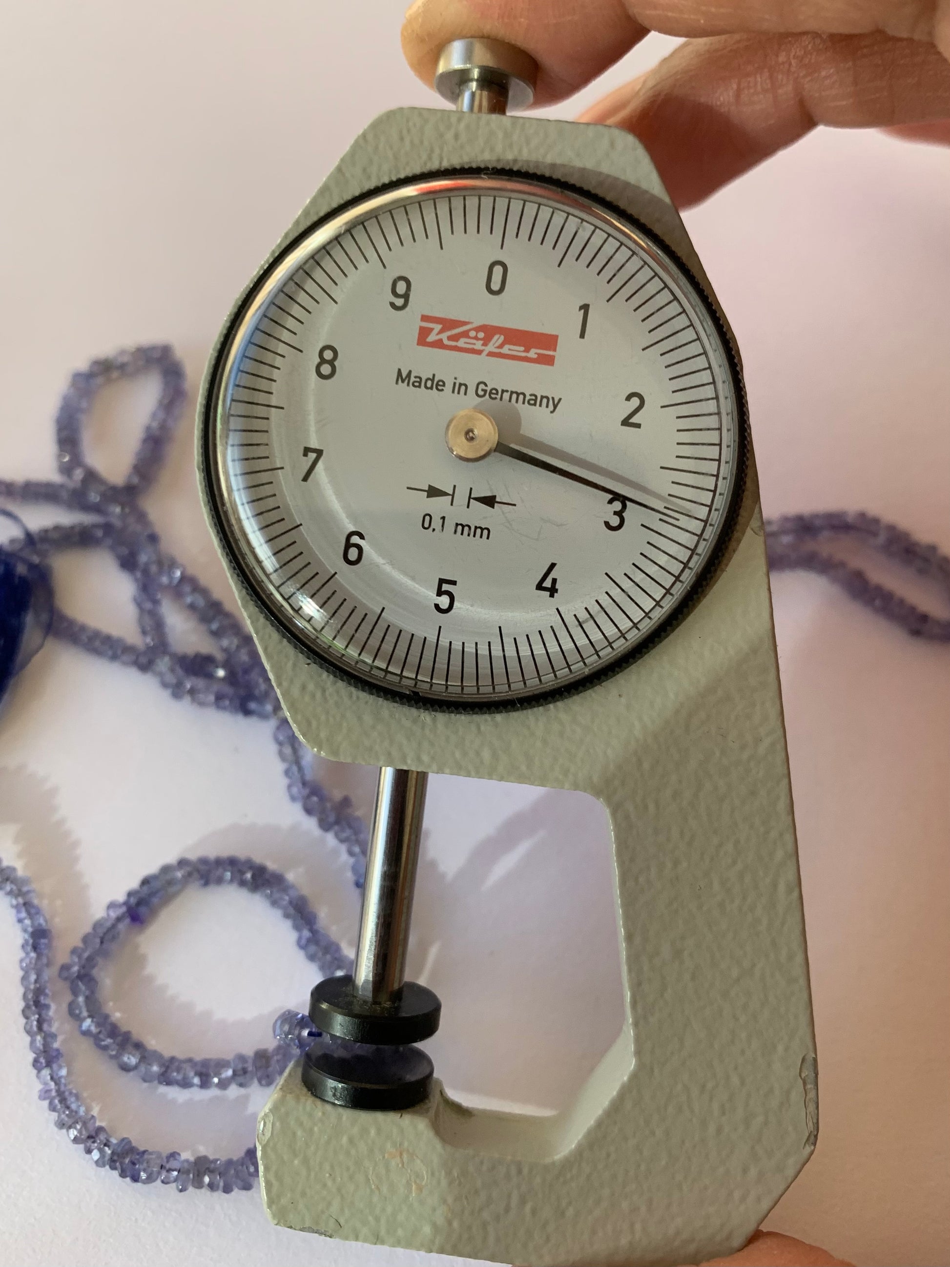 A person measuring a Tanzanite faceted rondelle bead with a dial gauge measure, showcasing its size and detail.