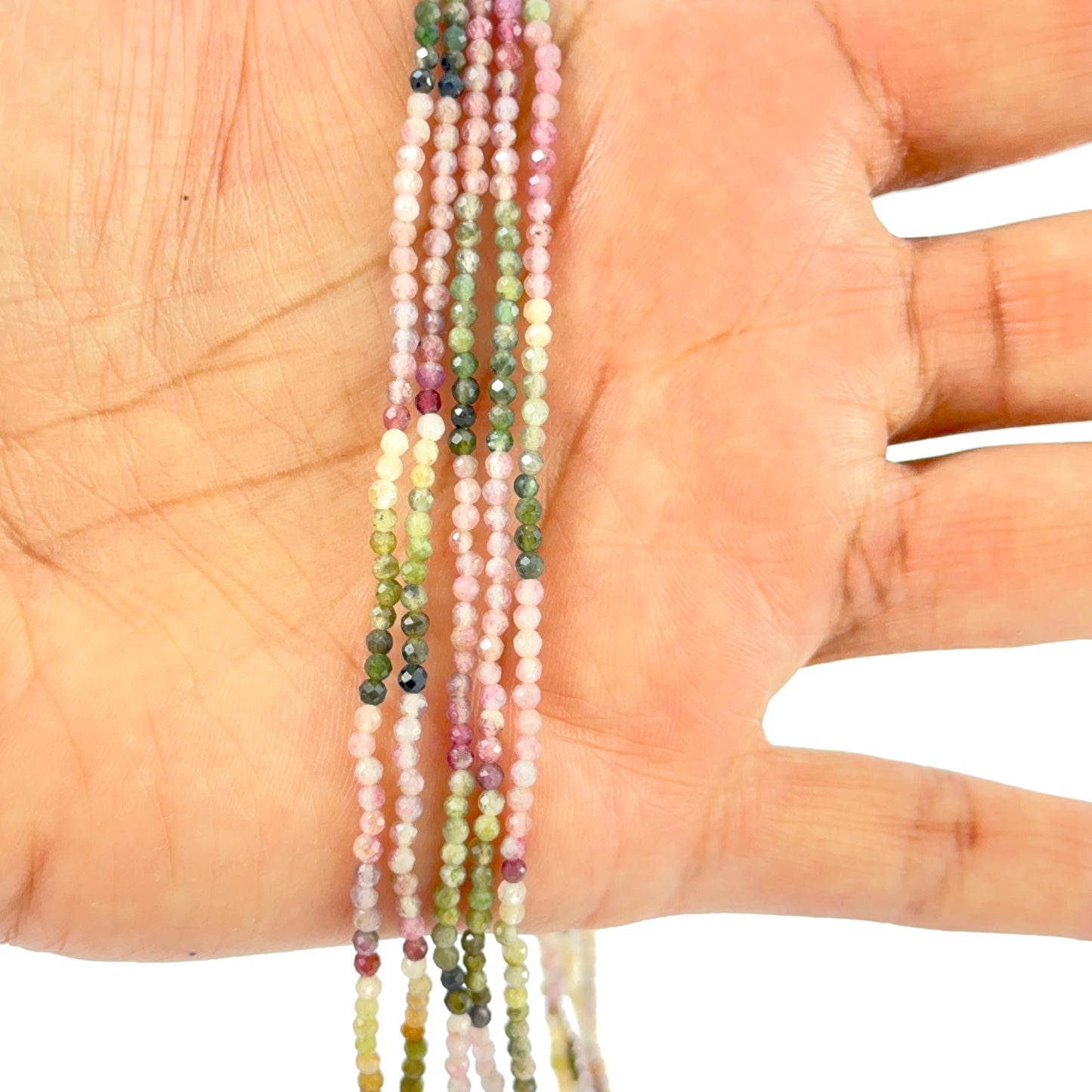 A person holds delicate strands of Tourmaline beads, showcasing their faceted design.