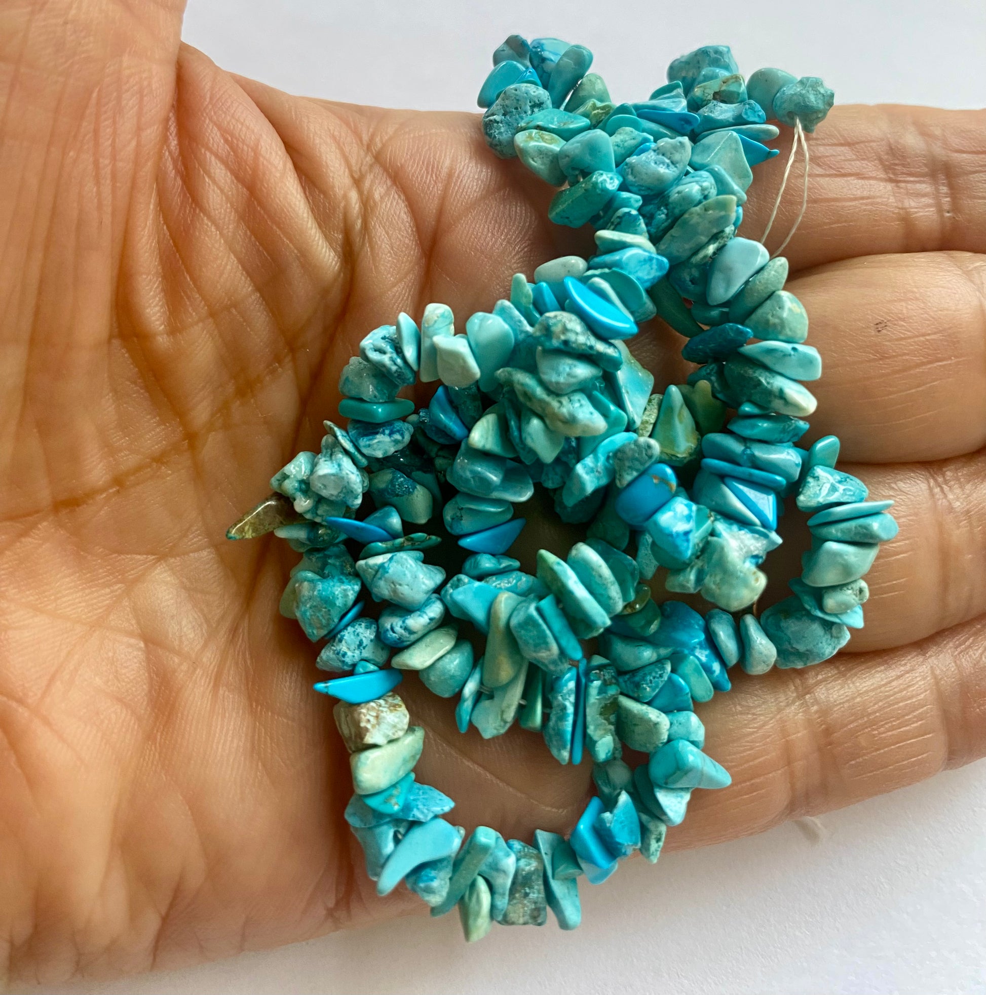 Close-up of a person holding a stunning tuquoise chip gemstone strand, highlighting its intricate facets.