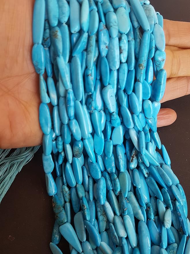 A hand presenting a group of smooth blue turquoise gemstone beads, sized between 6mm and 8mm, highlighting their beauty.