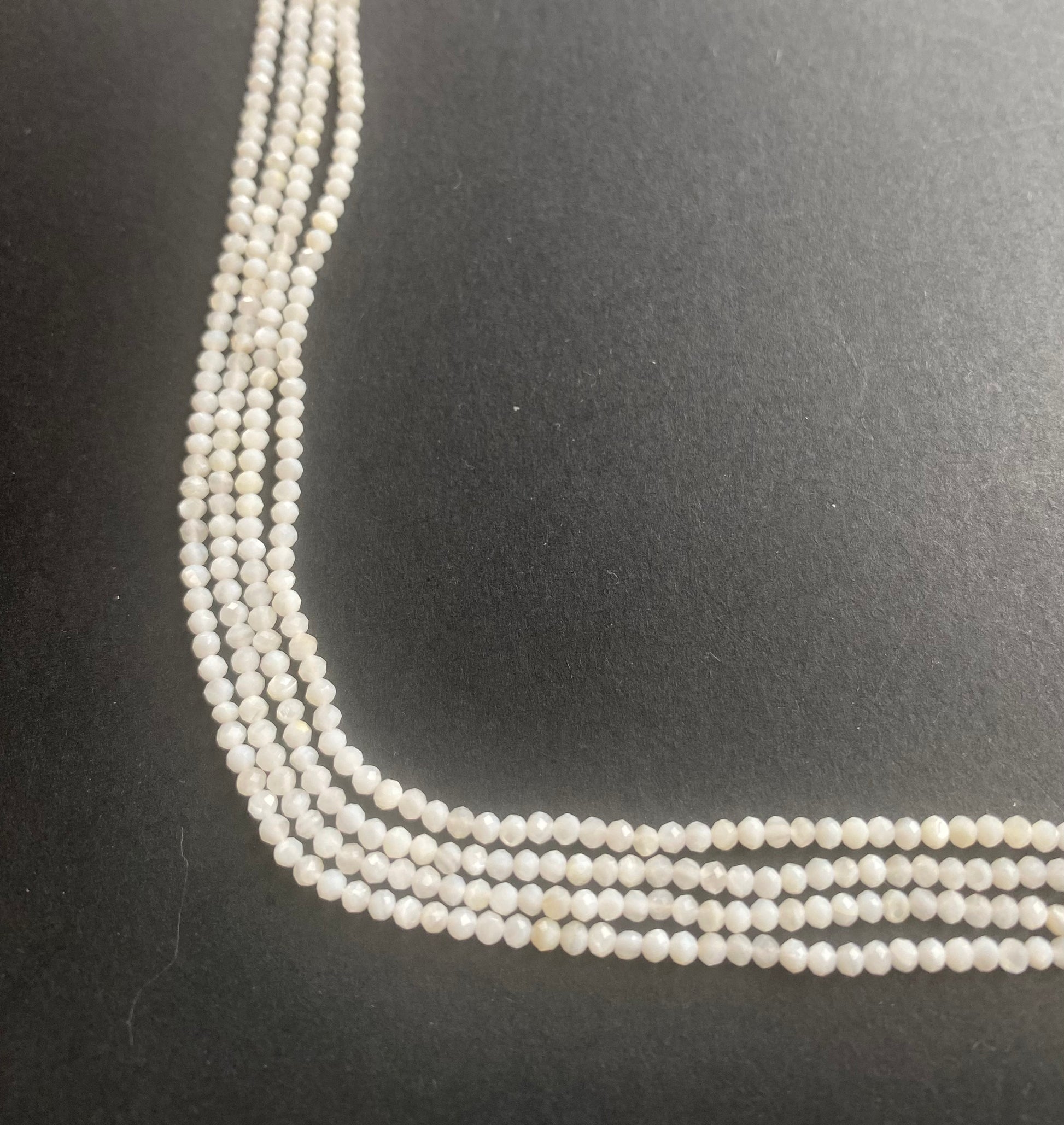 A close-up of a multiple strands of white opal gemstone beads, faceted rondelles ranging from 2.25mm to 2.5mm, glistening in the light.