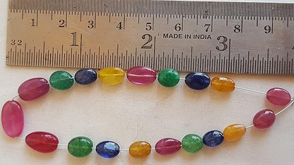 Close-up of a measuring ruler beside colourful multi-precious beads, including ruby, blue sapphire, yellow sapphire, and emerald.