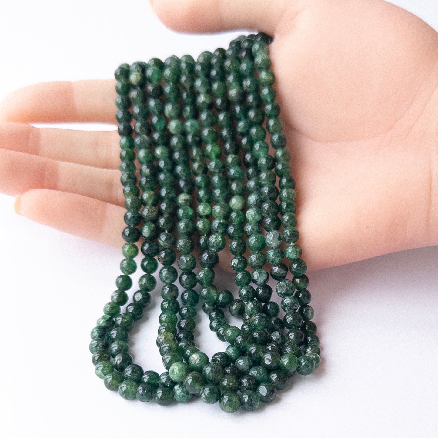 A person holds delicate strands of Aventurine beads, showcasing their smooth round design.