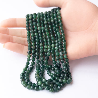 A person holds delicate strands of Aventurine beads, showcasing their smooth round design.