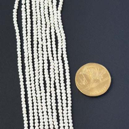 A coin place next to Freshwater pearl rondelles displayed on a strand to highlight their delicate shape and bright glow for scale.
