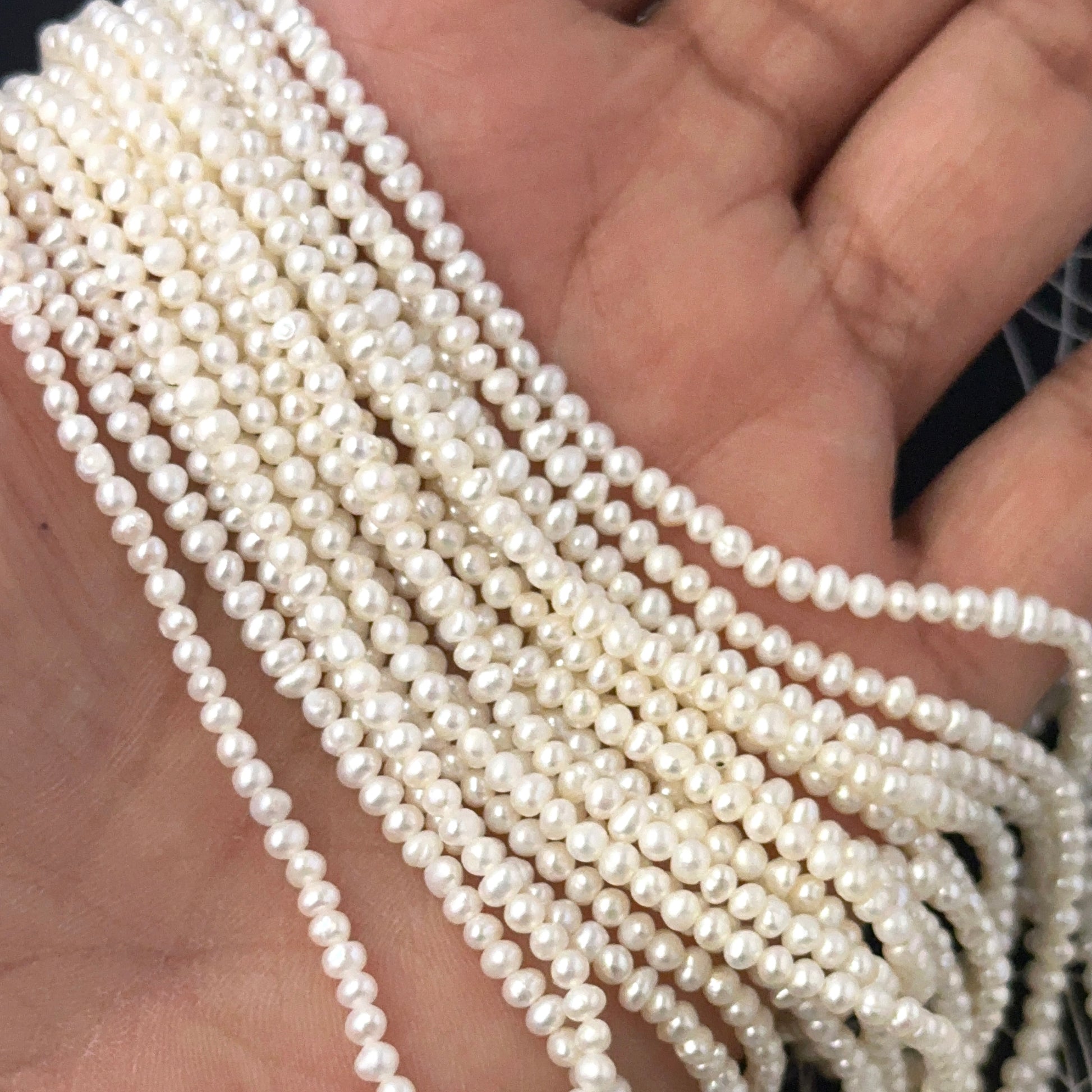 A person holds delicate strands of freshwater pearl beads, showcasing their smooth design.