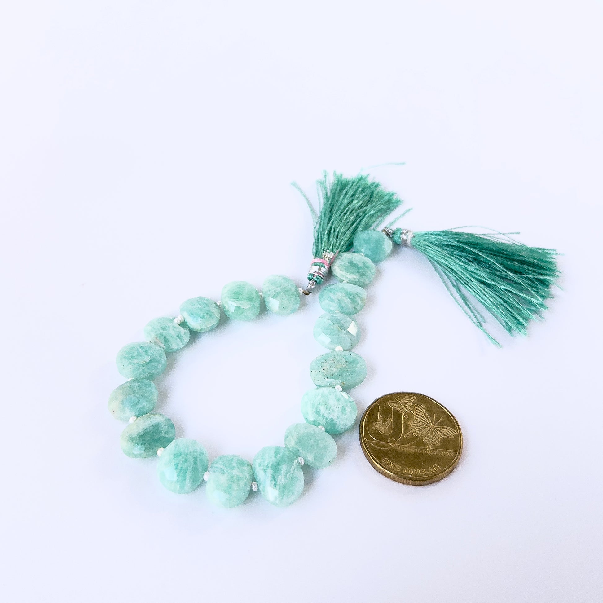 A coin is placed near delicate strands of Amazonite faceted briolette beads for scale.