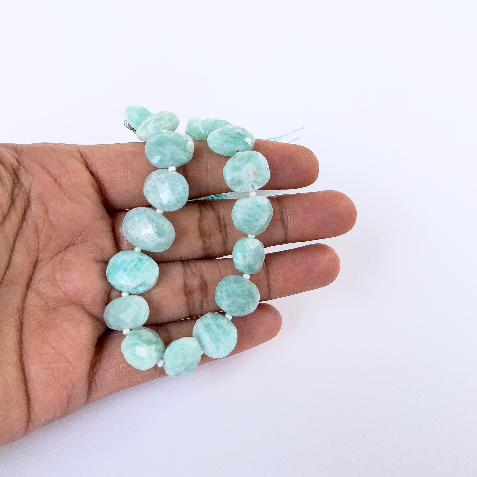 A person holds delicate strands of Amazonite faceted briolette beads, showcasing their cut design.