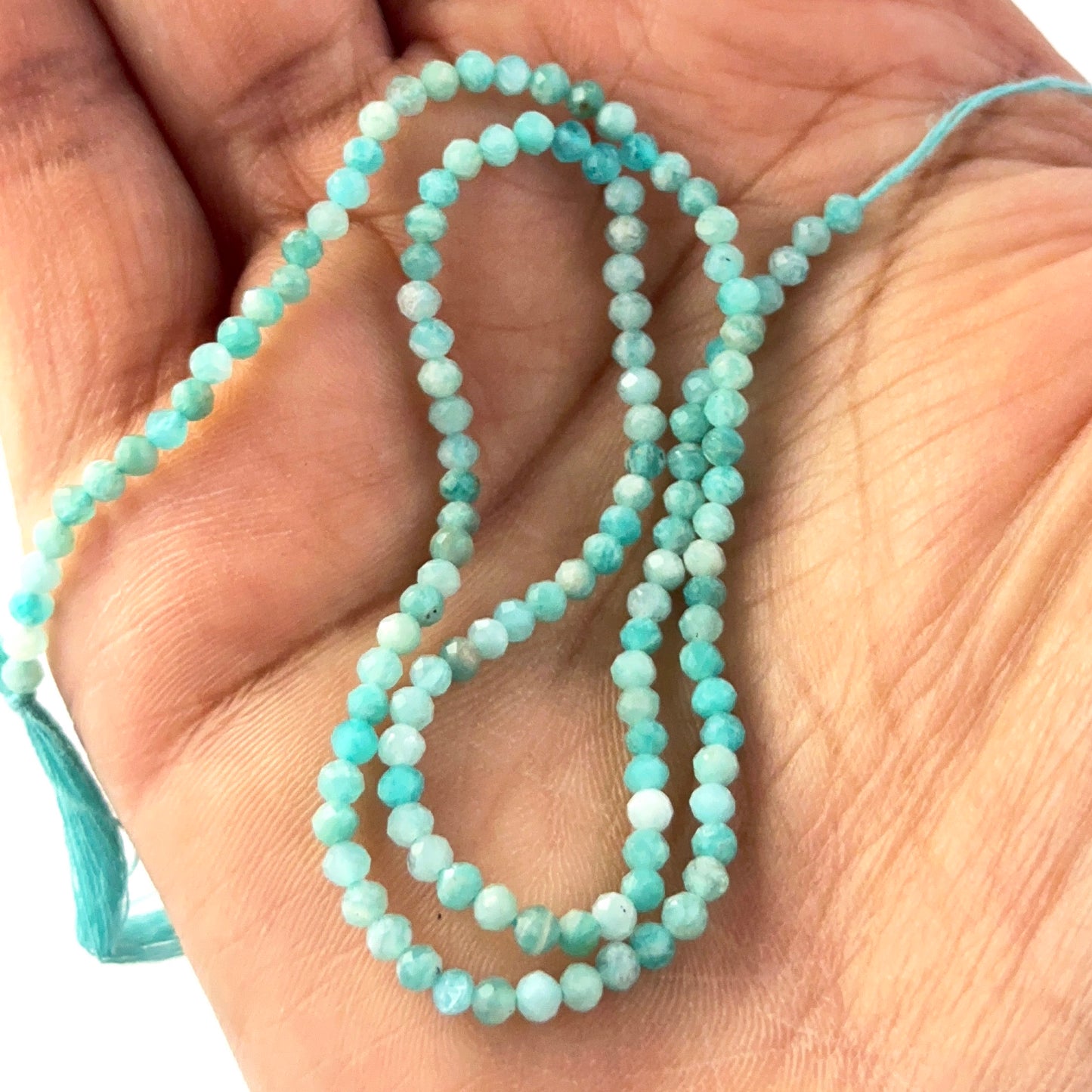 A person holds delicate strands of Amazonite beads, showcasing their faceted rondelle design.