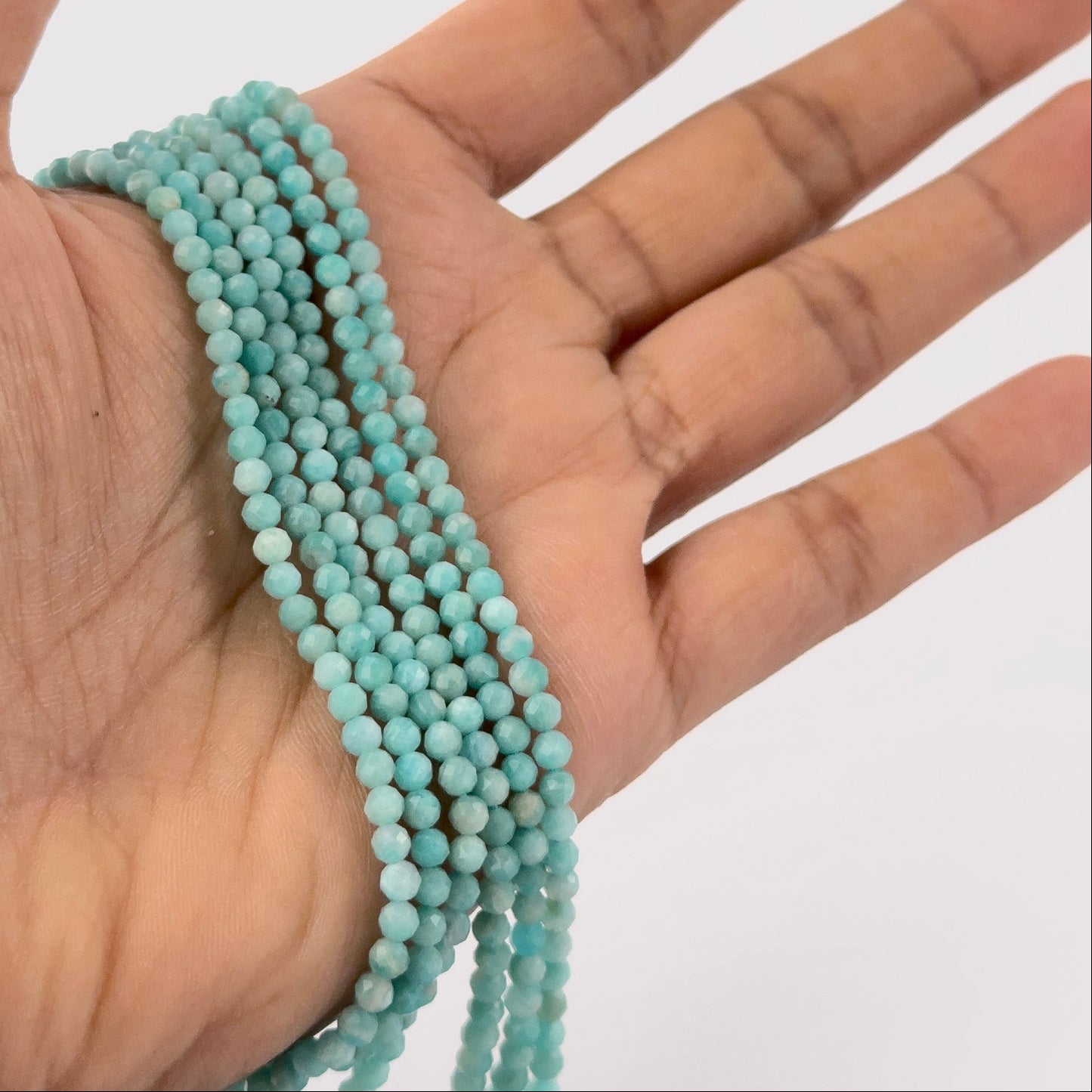 A person holds delicate strands of Amazonite beads, showcasing their faceted rondelle design.


