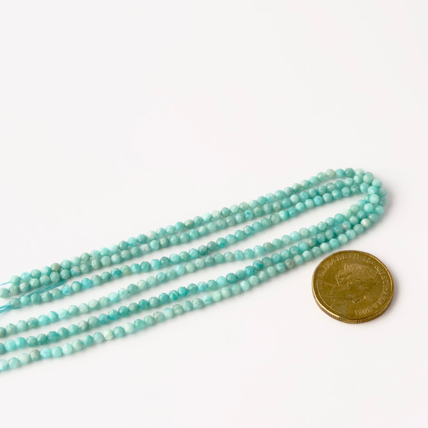 A coin is placed near delicate strands of Amazonite beads for scale