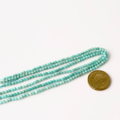 A coin is placed near delicate strands of Amazonite beads for scale