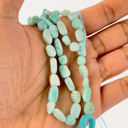 A person holds delicate strands of Amazonite beads, showcasing their tumble‑smooth design.
