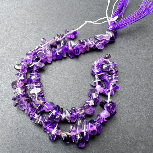 Amethyst smooth chip beads in varying purple tones arranged on a 23cm strand for jewellery making.
