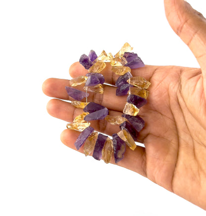 A person holds Amethyst and Citrine drilled rough beads, showing their natural raw formation and colour variation.