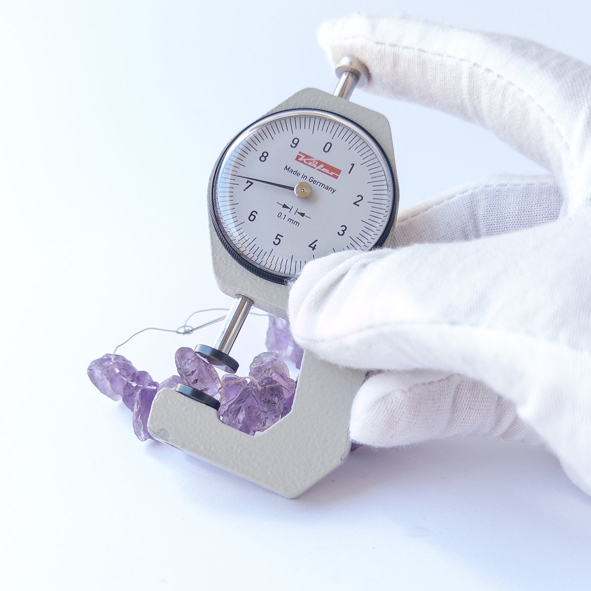 A dial gauge measures the Amethyst drilled rough 7.5–11mm gemstone.