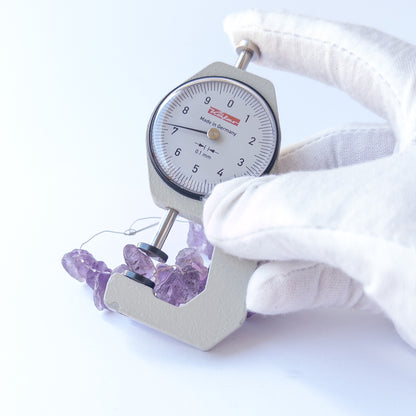 A dial gauge measures the Amethyst drilled rough 7.5–11mm gemstone.