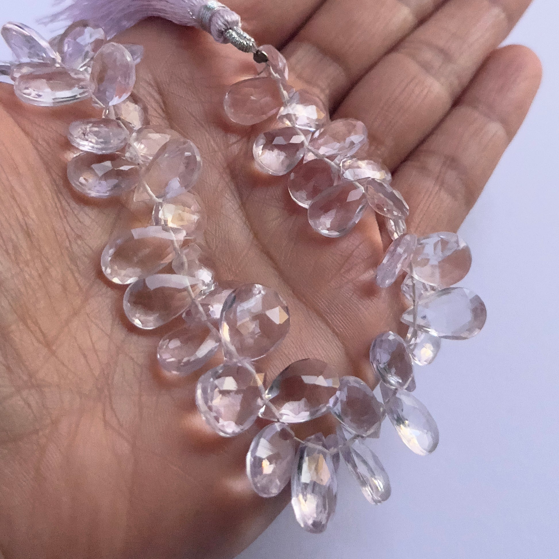 A person holds delicate strands of Amethyst beads, showcasing their smooth design.