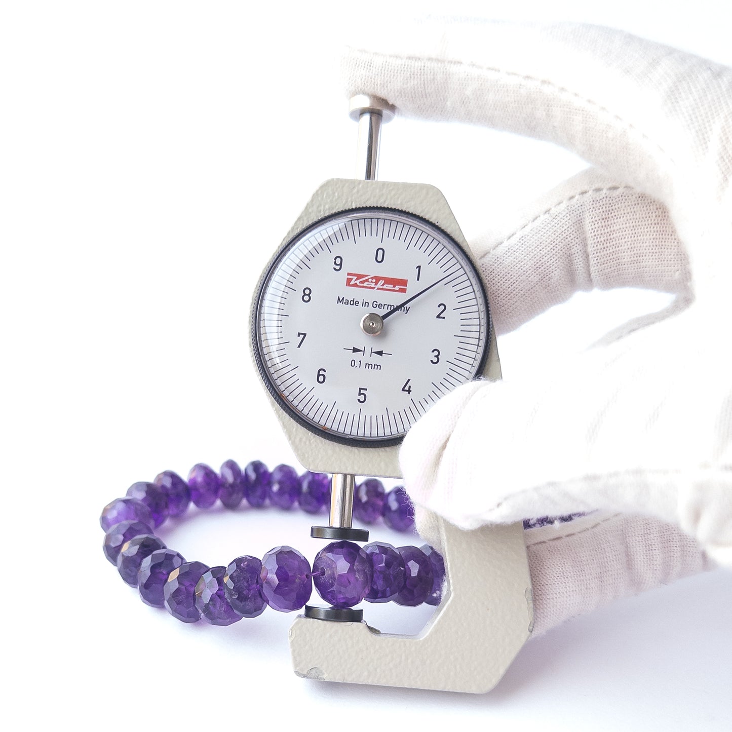 A dial gauge measures the Amethyst faceted rondelle 10.2–11mm gemstone.