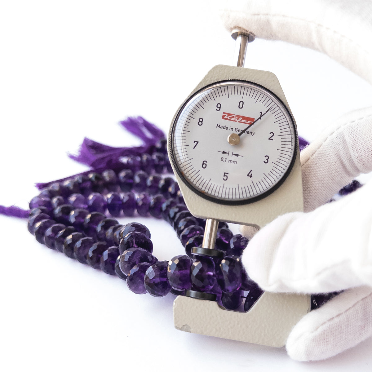 A dial gauge measures the Amethyst faceted rondelle 10.5–11.5mm gemstone.