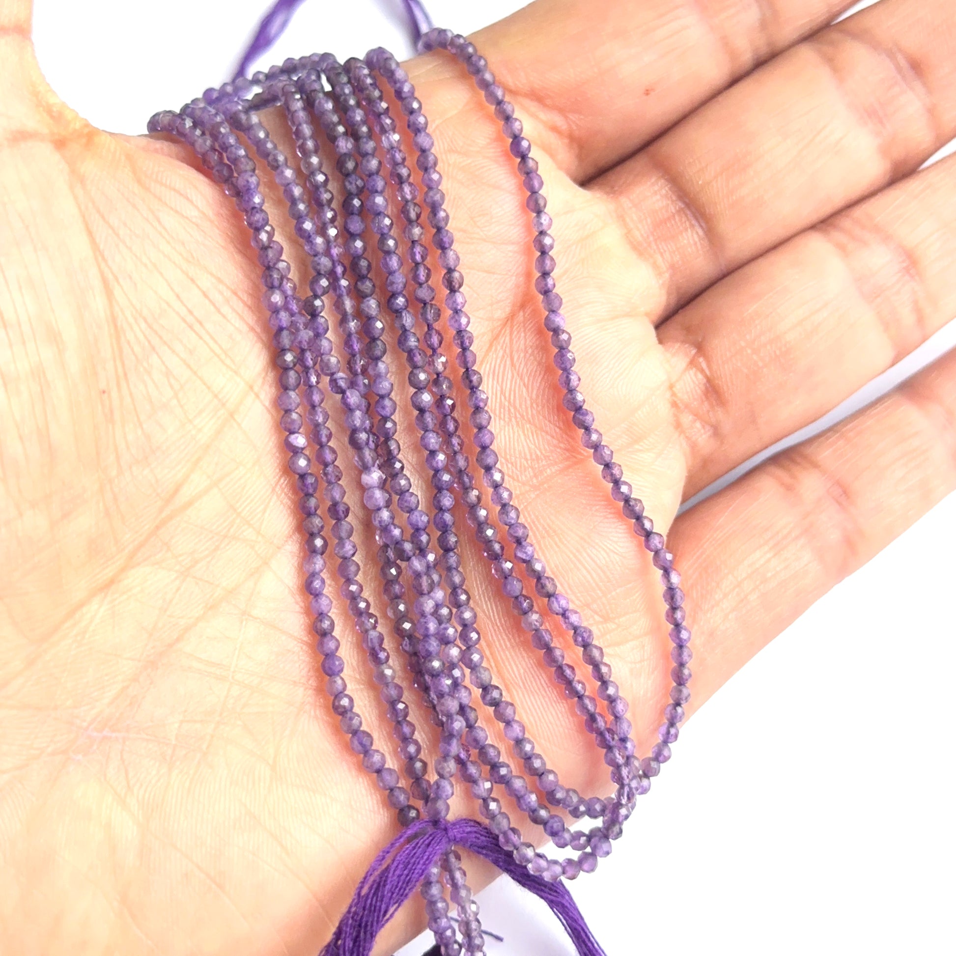 A person holds delicate strands of amethyst faceted beads, showcasing their smooth design.