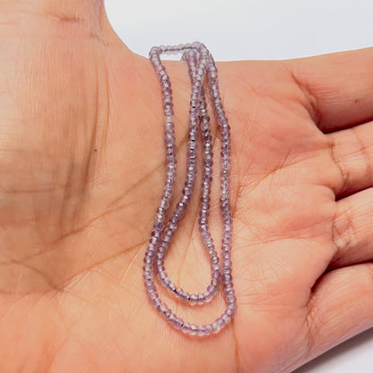 A person holds delicate strands of Amethyst beads, showcasing their smooth design.