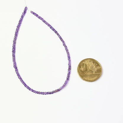 A coin is place near delicate strands of Amethyst beads for scale.