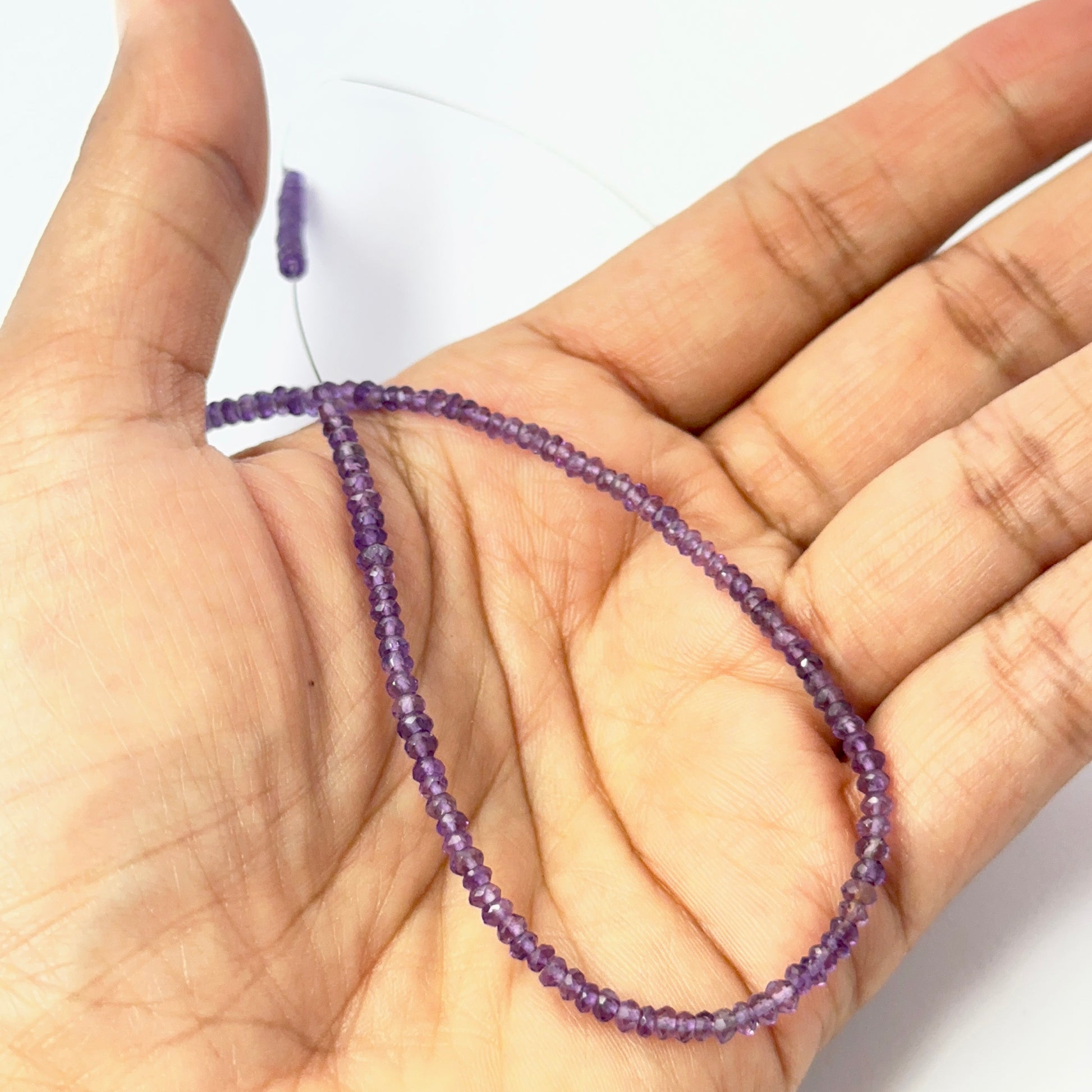 A person holds delicate strands of Amethyst beads, showcasing their faceted rondelle design.