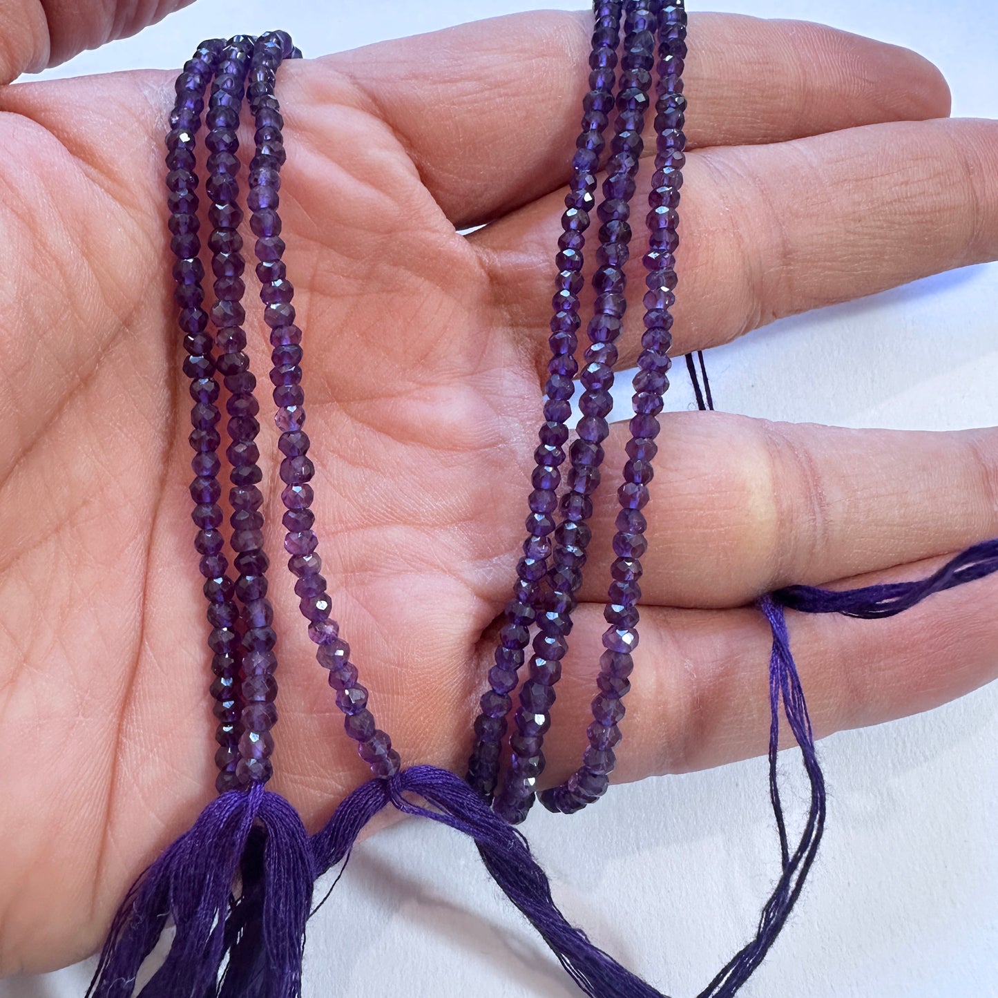 A person holds delicate strands of amethyst beads, showcasing their smooth design.