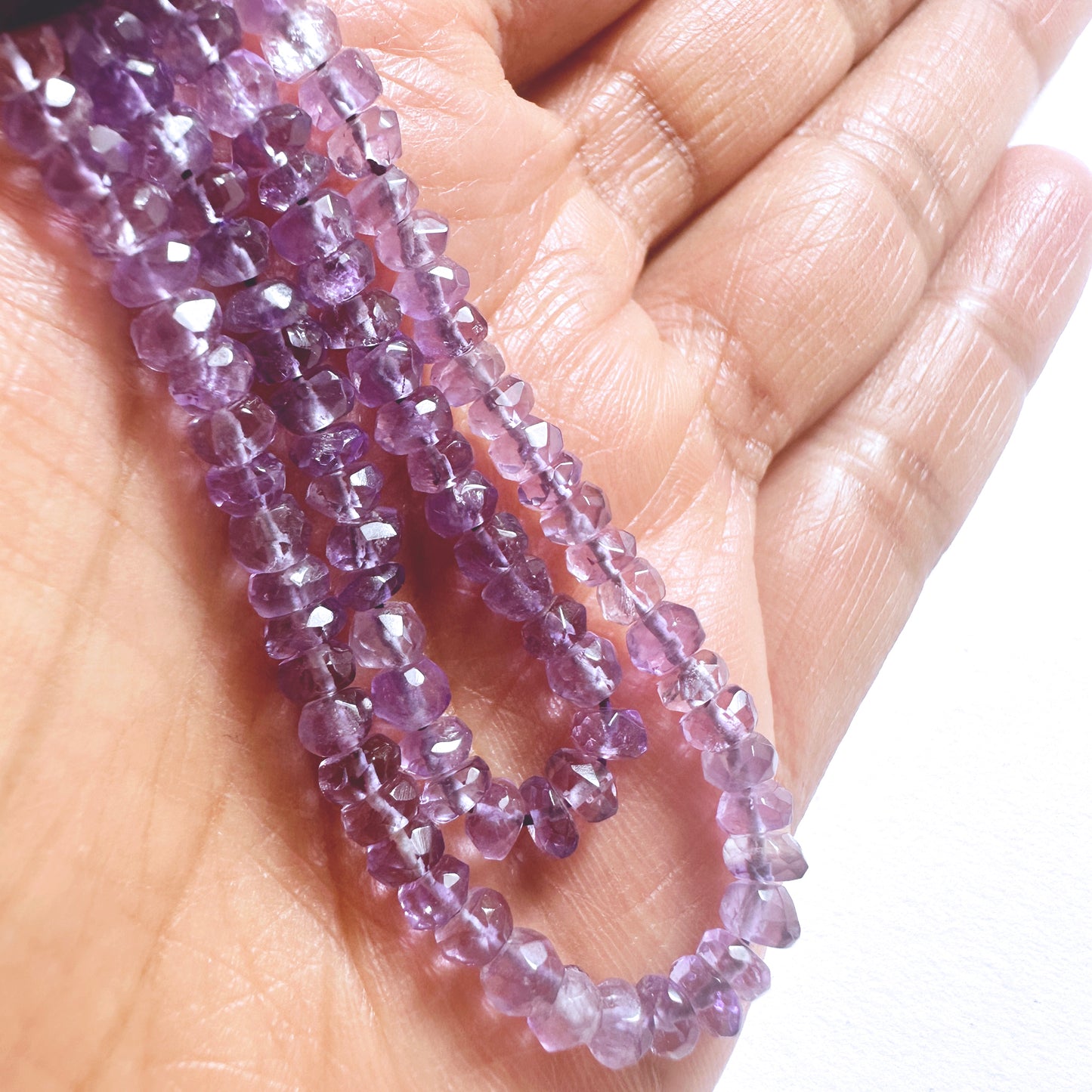 A person holds delicate strands of Amethyst beads, showcasing their smooth design.