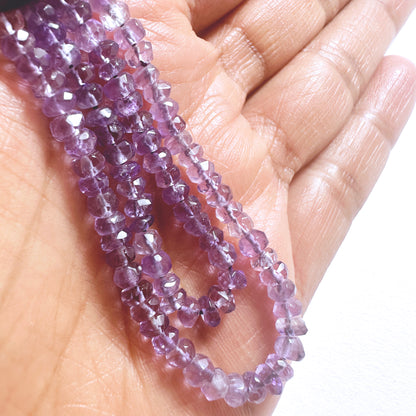 A person holds delicate strands of Amethyst beads, showcasing their smooth design.