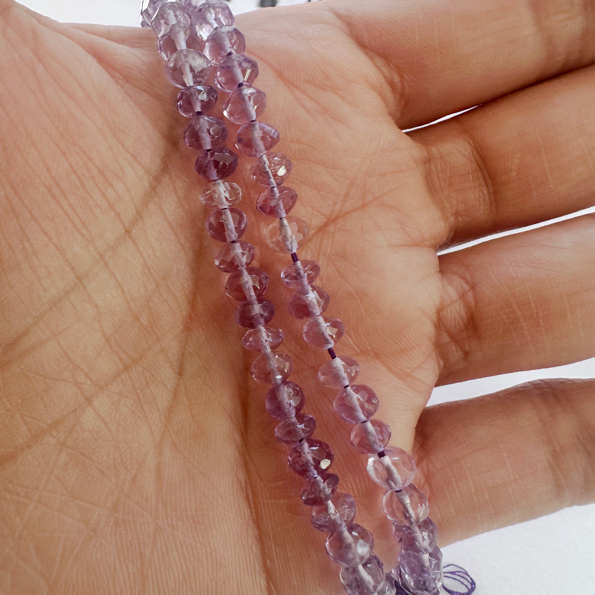 A person holds delicate strands of Amethyst beads, showcasing their smooth design.