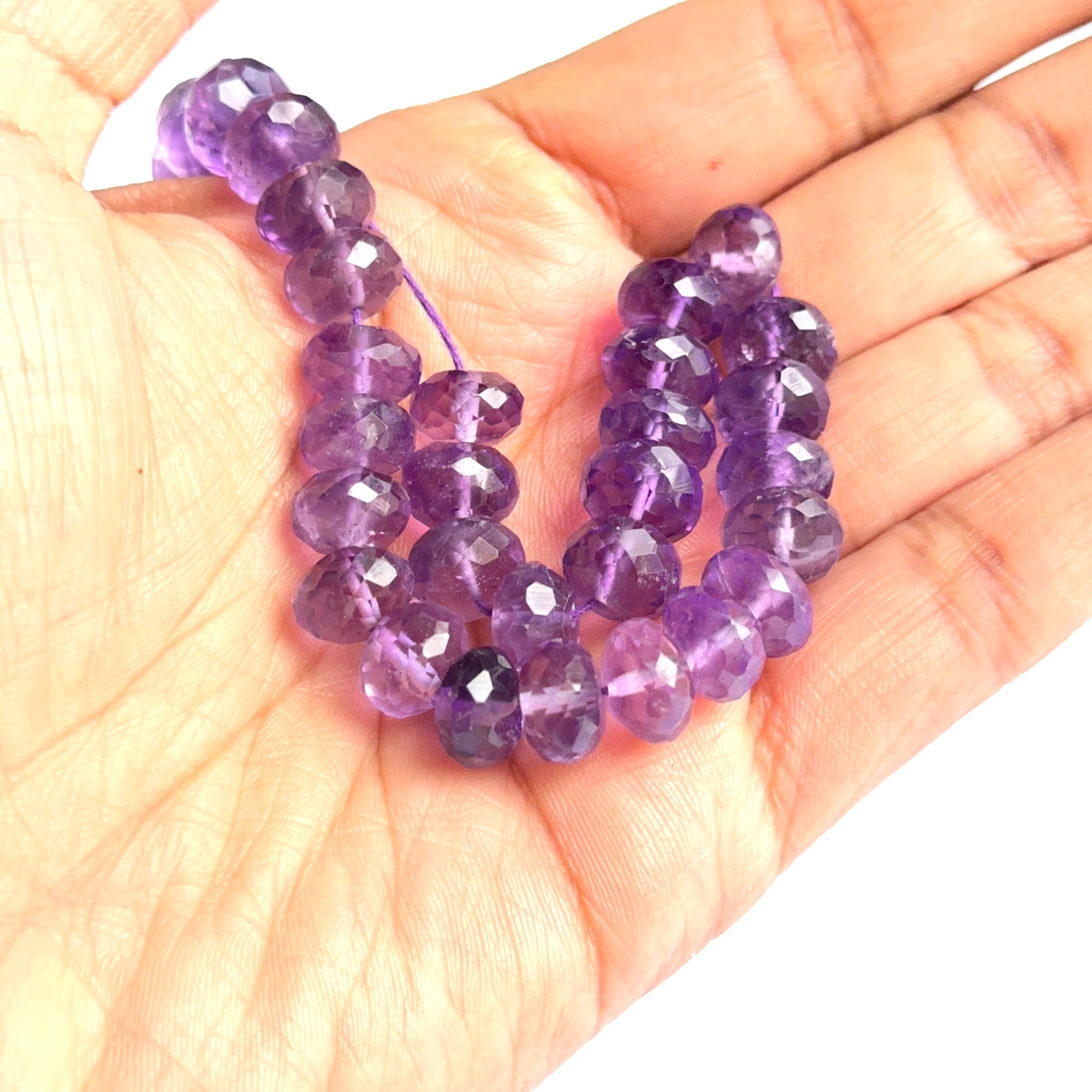 A person holds delicate strands of amethyst faceted beads, showcasing their smooth design.